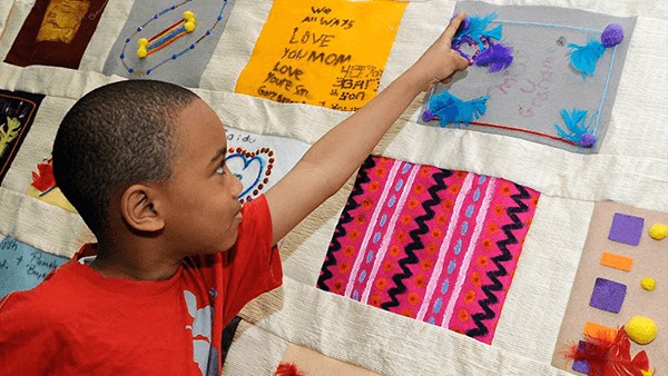 Young Boy Placing Feathers on Fabric Art Piece