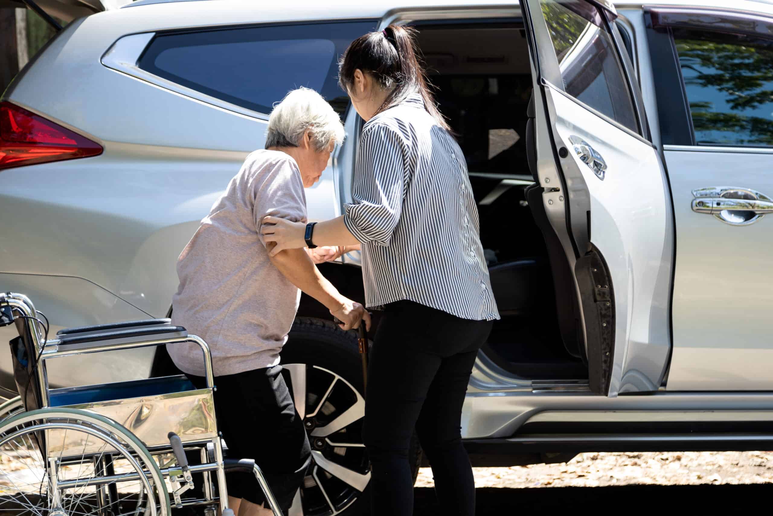 Woman helping older adult get into car