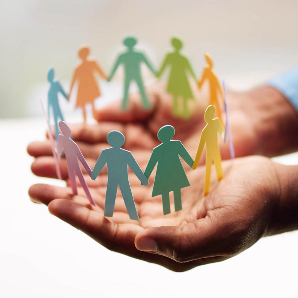 A pair of hands cupped together, holding a colorful ring of interconnected paper human figures representing community and unity.